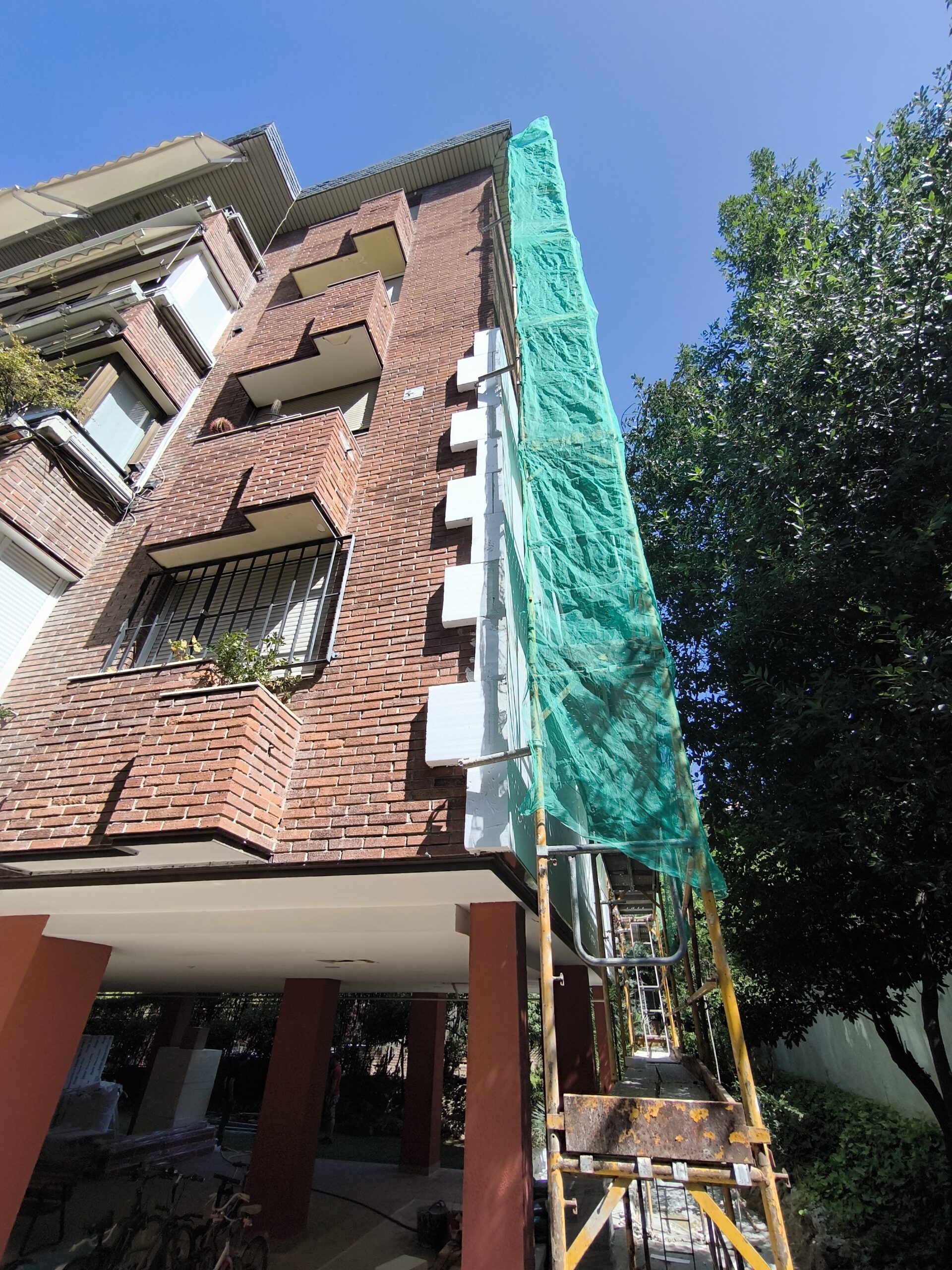 Aleixandre 4. Julio de 2025 · Colocación del aislamiento exterior en el encuentro de esquina, con andamio y malla de protección.